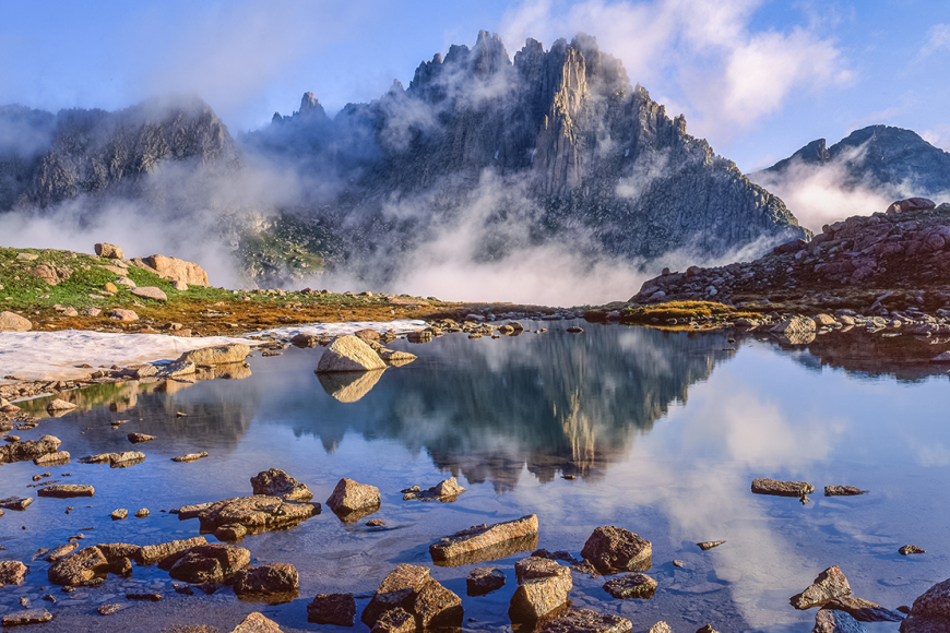 Jagged Mountain surrounded by fog, Weminuche Wilderness. Rocks reflect off the crystal clear pond in the foreground.