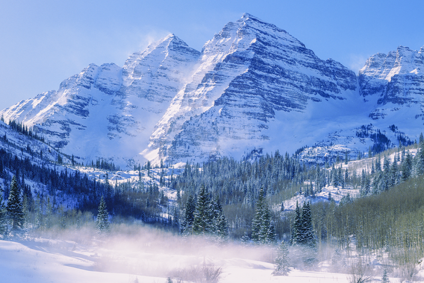 Maroon Bells snowy mountain peak surrounded by pine trees and a snow covered valley,