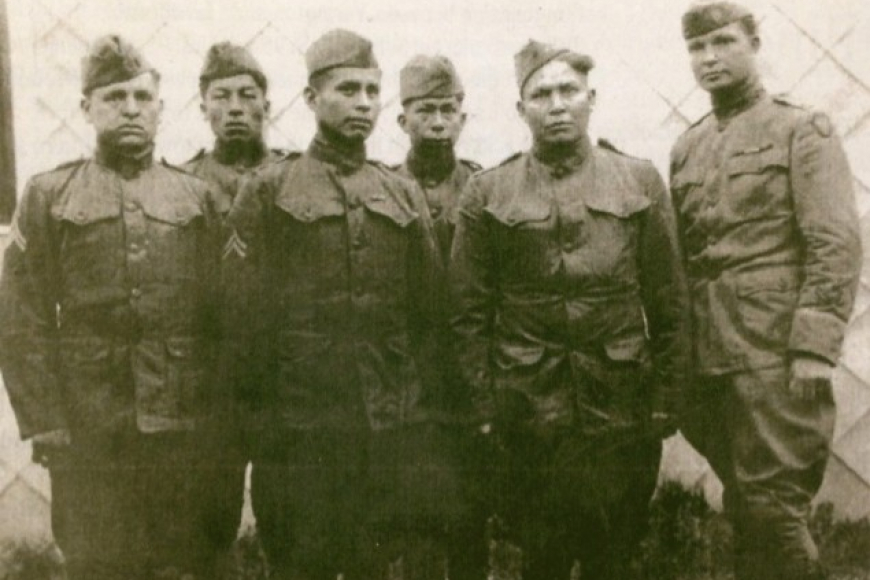 A group of soldiers, part of the 45th Infantry: 36th Division Code Talkers stand in a group of 6 and look seriously at the camera.