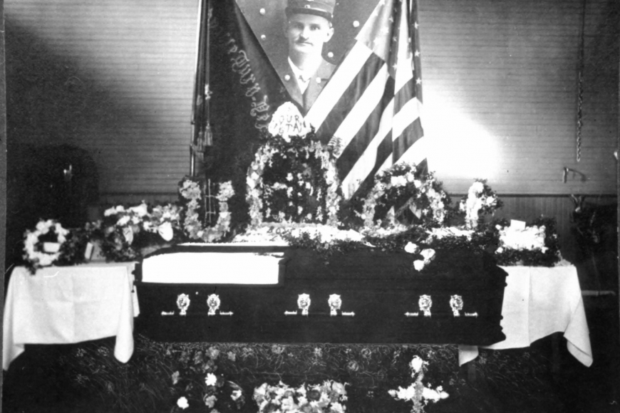 Leadville fireman Max Hahnewald’s casket surrounded by flowers sits in front of flags and his portrait.