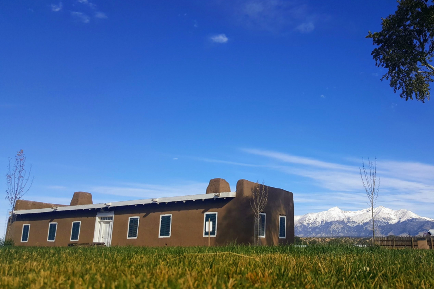 Exterior of Fort Garland with snow-capped mountains behind an adobe building.