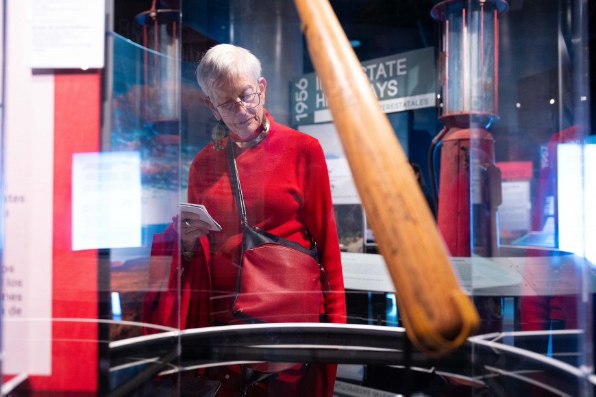 An older female guests reads a label in front of Jackie Robinson's historic baseball bat.
