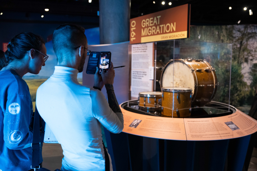 1 guests take a photo of the Great Migration display and drum set at the exhibition.