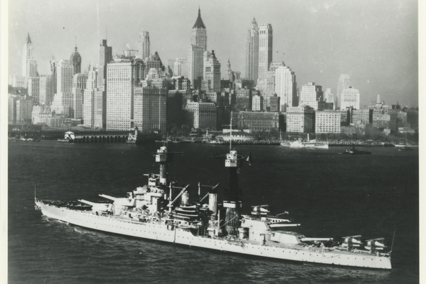 USS Colorado floating in water with New York City skyline in distance.
