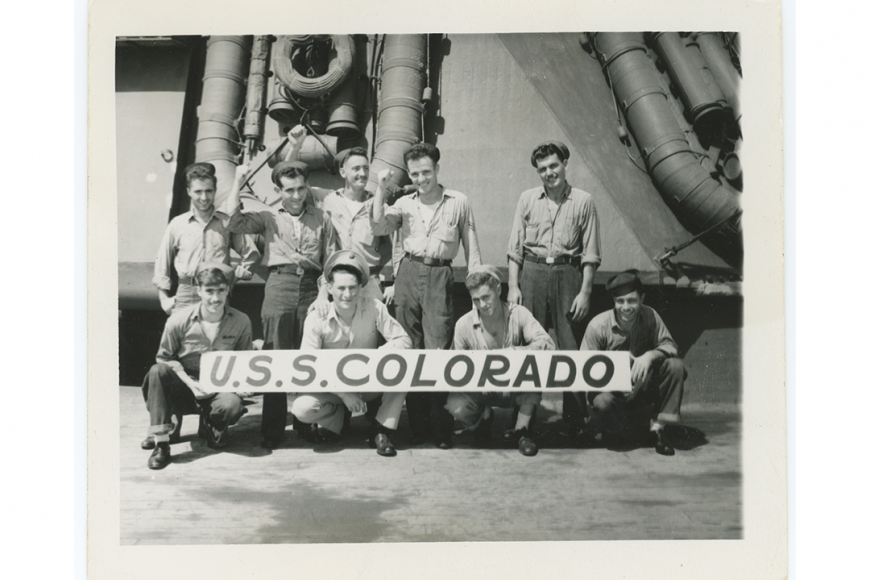 USS Colorado crew standing in a group of nine people holding a banner that reads USS Colorado.
