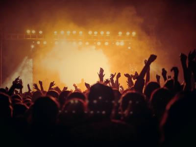 Photo of an illuminated concert stage filled with smoke, and the silouettes of concert-goers in the foreground.