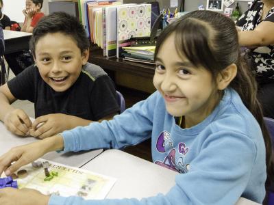 Photo of two elementary students, sitting at a desk together, smiling and playing a game based on the history of Silverton, Colorado.