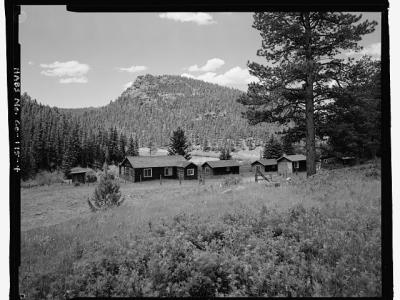 Photo of the McGraw Ranch buildings. In a clearing adjacent to large pine trees, sit three guest cabins and the laundry building, all of one-story log cabin design.