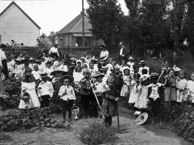 Kindergarten students at Bessemer School working in their school garden, 1902. Adults behind the class include teachers Miss Carrie Carlile, Miss Mary Williamson, and another unknown woman, most likely another teacher and Superintendent J. F. Keating.