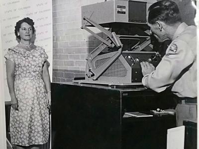 A woman poses in front of an antique camera.