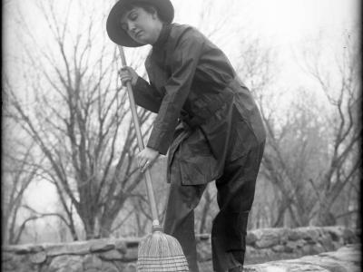 A woman dressed as a witch and holding a wicker broom in a vintage Halloween photograph.