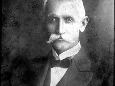 Black and white studio portrait of a man in a suit with a mustache looking into the camera