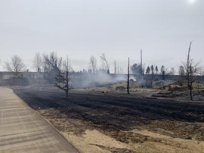 The remains of a burnt structure still smoking, and a black burn scar with charred trees surrounding it.