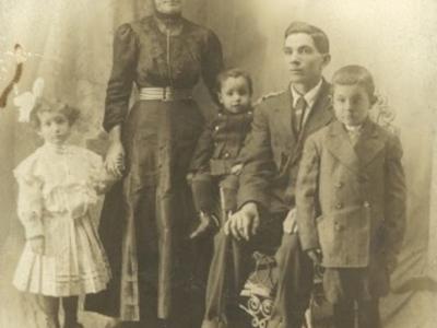 A faded, black and white photo of the Costa Family, with a woman and two children standing while a man is sitting