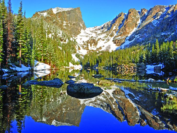 A lake with crystal clear water surrounded by trees and snow capped peaks in Rocky Mountain National Park