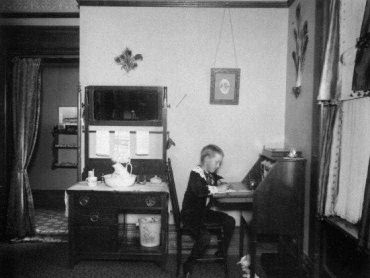 Child writing at desk, 1890-1900
