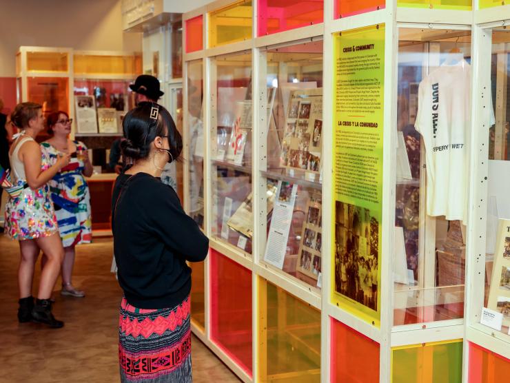 A woman looks at the multi-colored glass information and artifact cases making up Rainbows & Revolutions