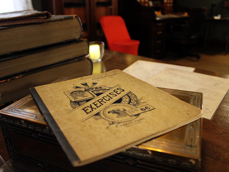 Stack of books on a wooden table. At the top, an old pamphlet reads 'Exercises.'