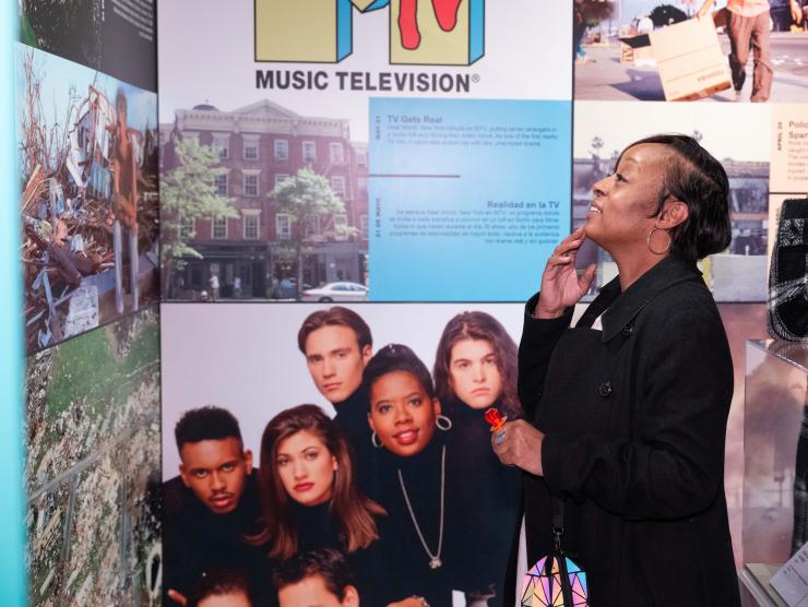 A guest in the 90s exhibit reads a panel with interest. Behind her is the MTV logo and other pop culture iconography.