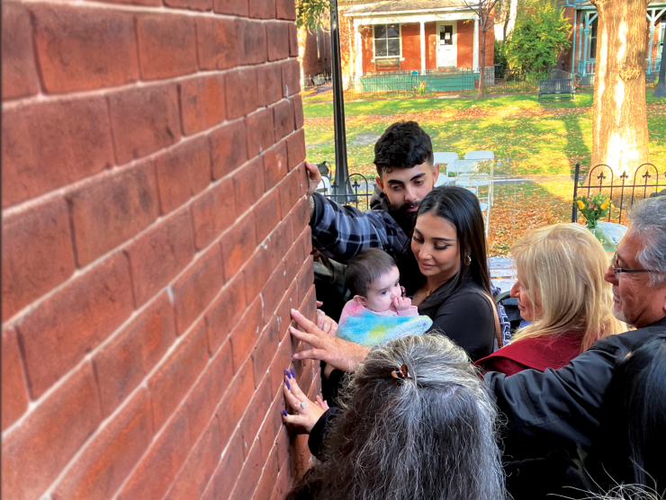 A family stands together and presses hands to a brick wall.