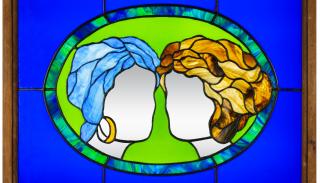 A stained glass window, depicting two women's heads facing each other. One has blue hair, the other has blonde hair. They are faceless.