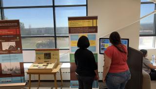 Two women reading a pop-up panel about Ute knowledge, in front of a large window.