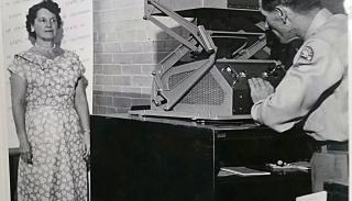 A woman poses in front of an antique camera.