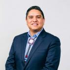 Portrait photograph of Ernest House, Jr. He wears a beaded bolo tie, button down collared shirt, and a dark navy or black jacket.