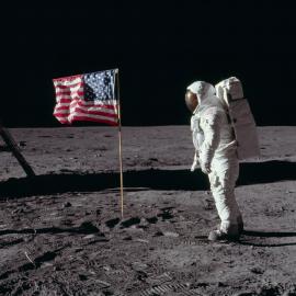 Buzz Aldrin in a space suit on the moon next to an American Flag