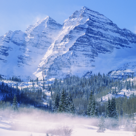 Maroon Bells snowy mountain peak surrounded by pine trees and a snow covered valley,