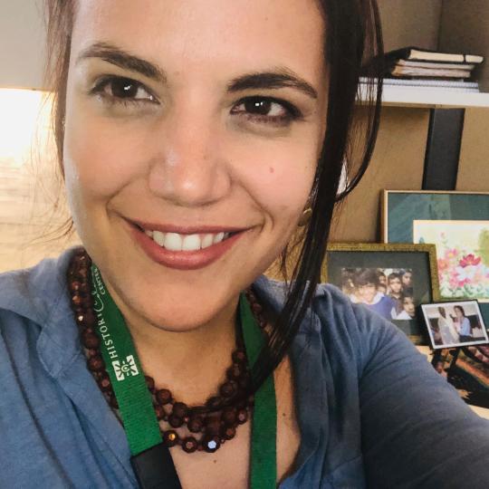 Photograph of Marissa Volpe at her desk in Denver. There are framed photographs in the background and books decorating her office.